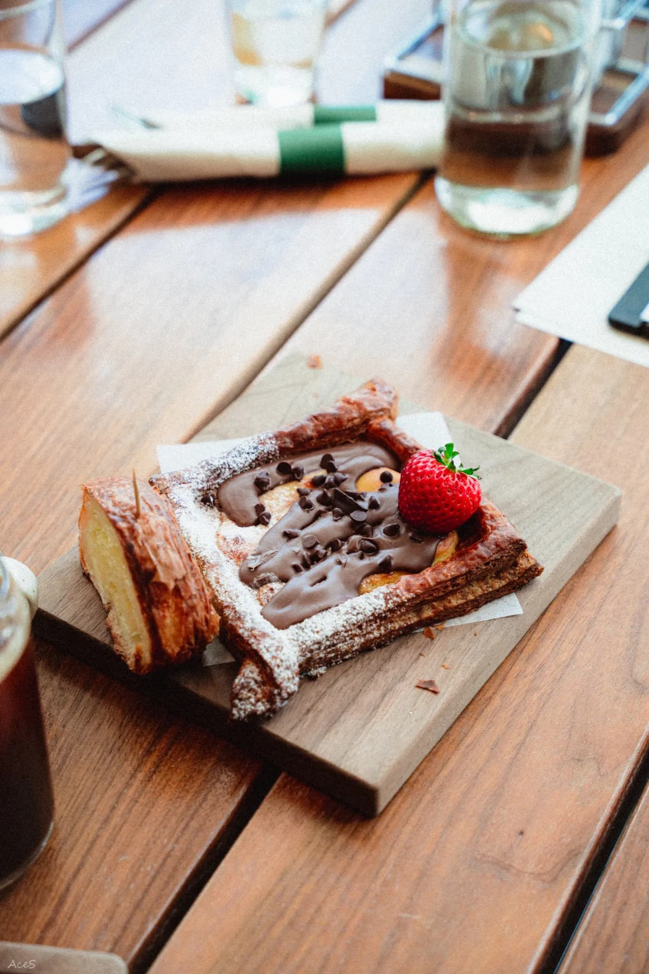 Chocolate pastry with fresh strawberry on wooden cutting board at outdoor cafe table