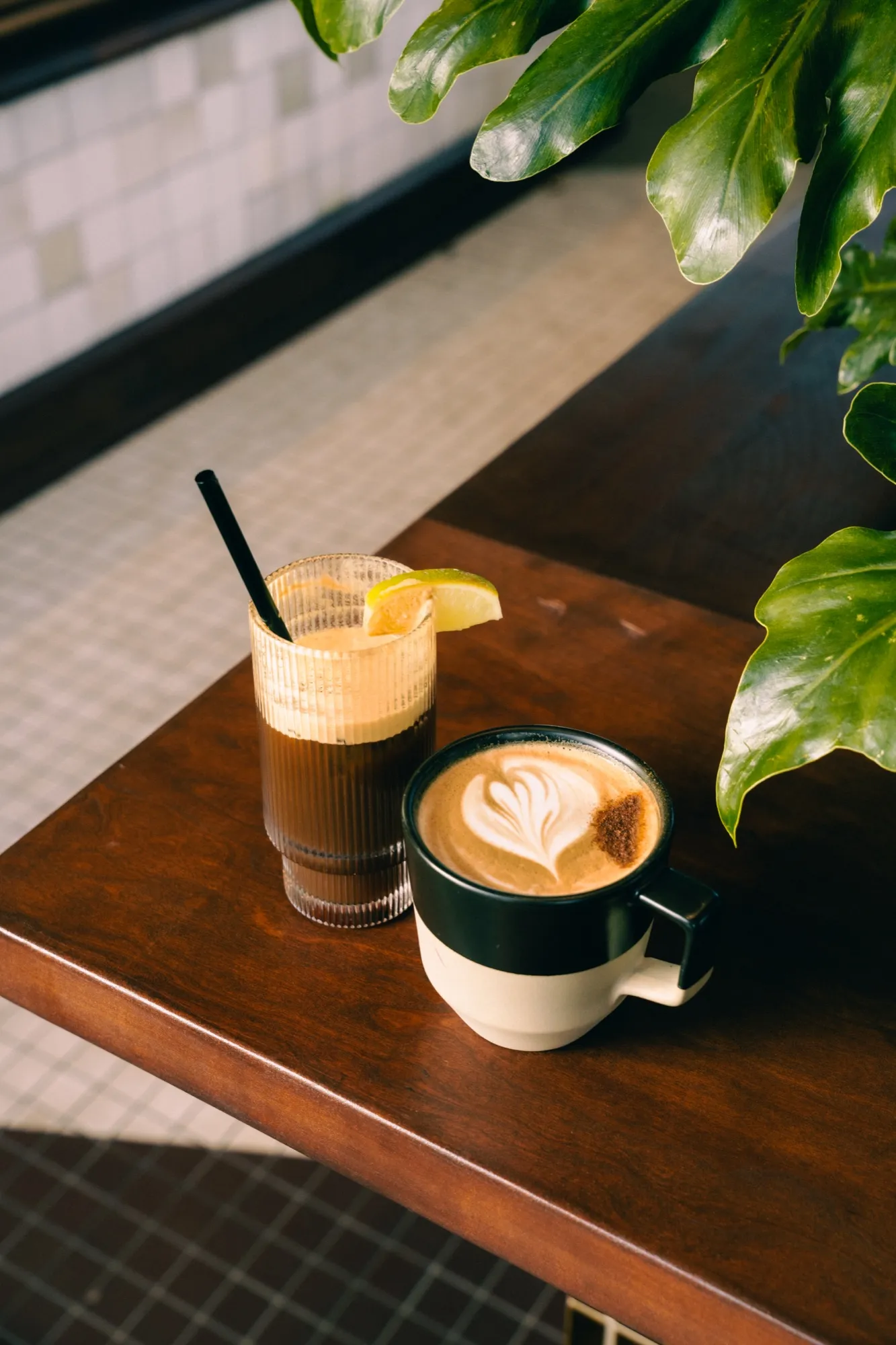 Iced lemon coffee drink and latte art on wooden cafe table with greenery